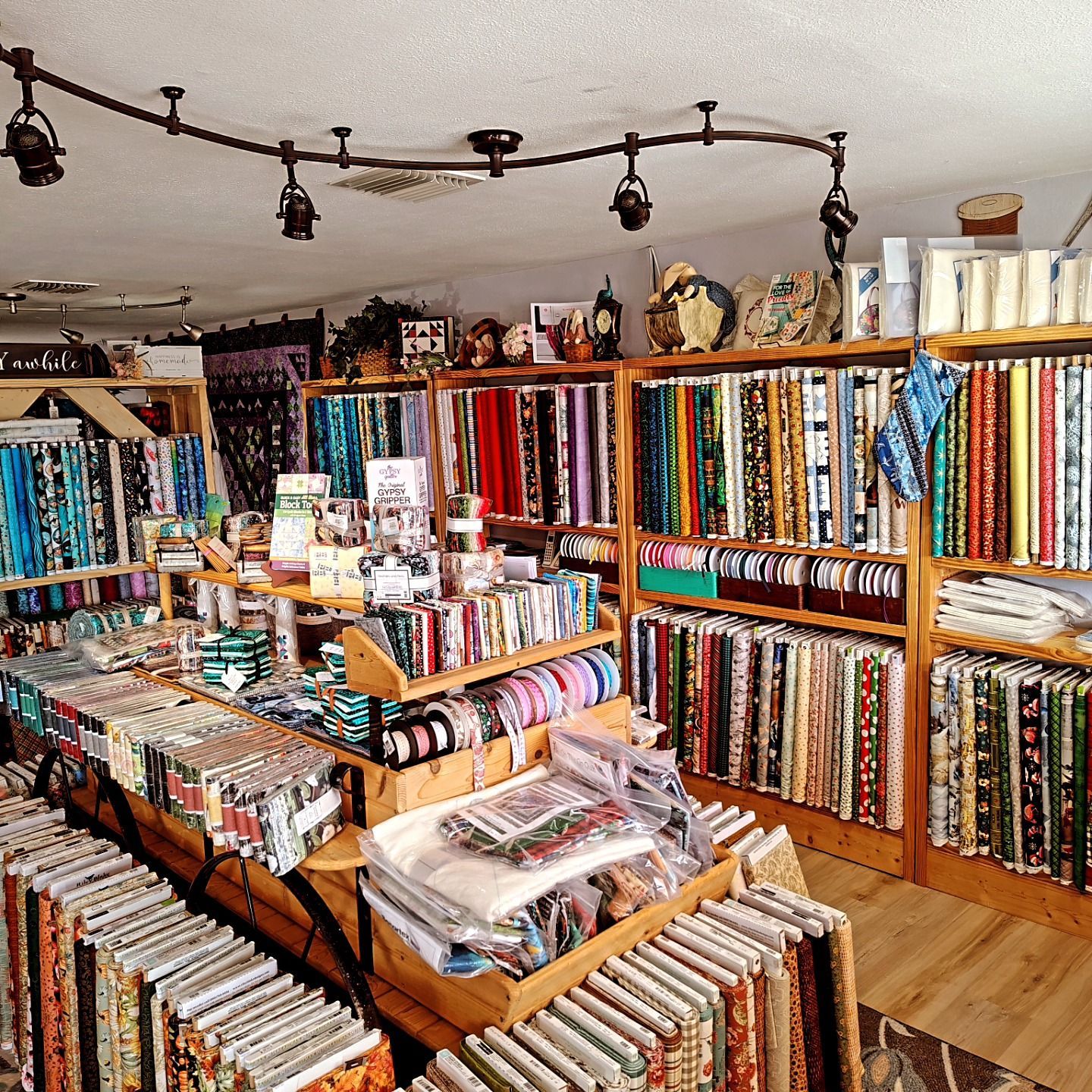 Bright fabric shop with shelves of colorful bolts, ribbons, and craft supplies on wooden racks