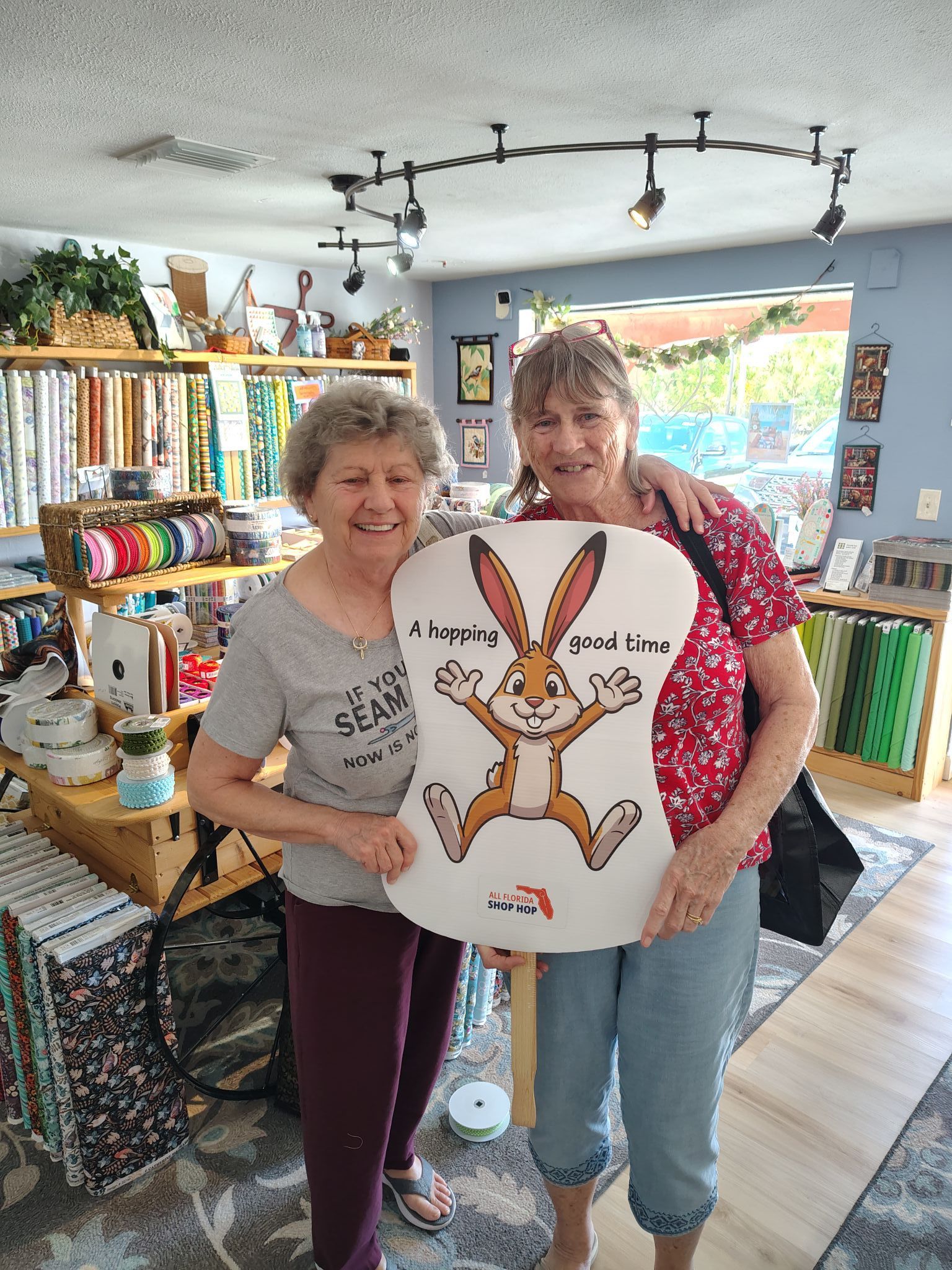 Two women holding a large rabbit artwork inside a bright, colorful shop