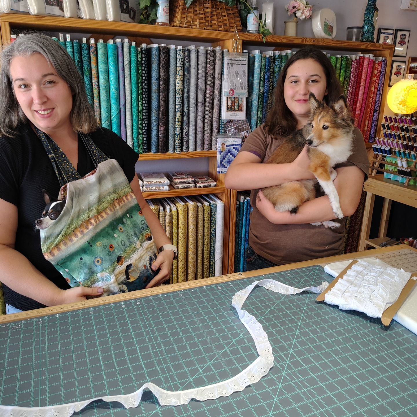 Two women in a fabric shop, one holding a cat and the other holding a colorful fabric piece.