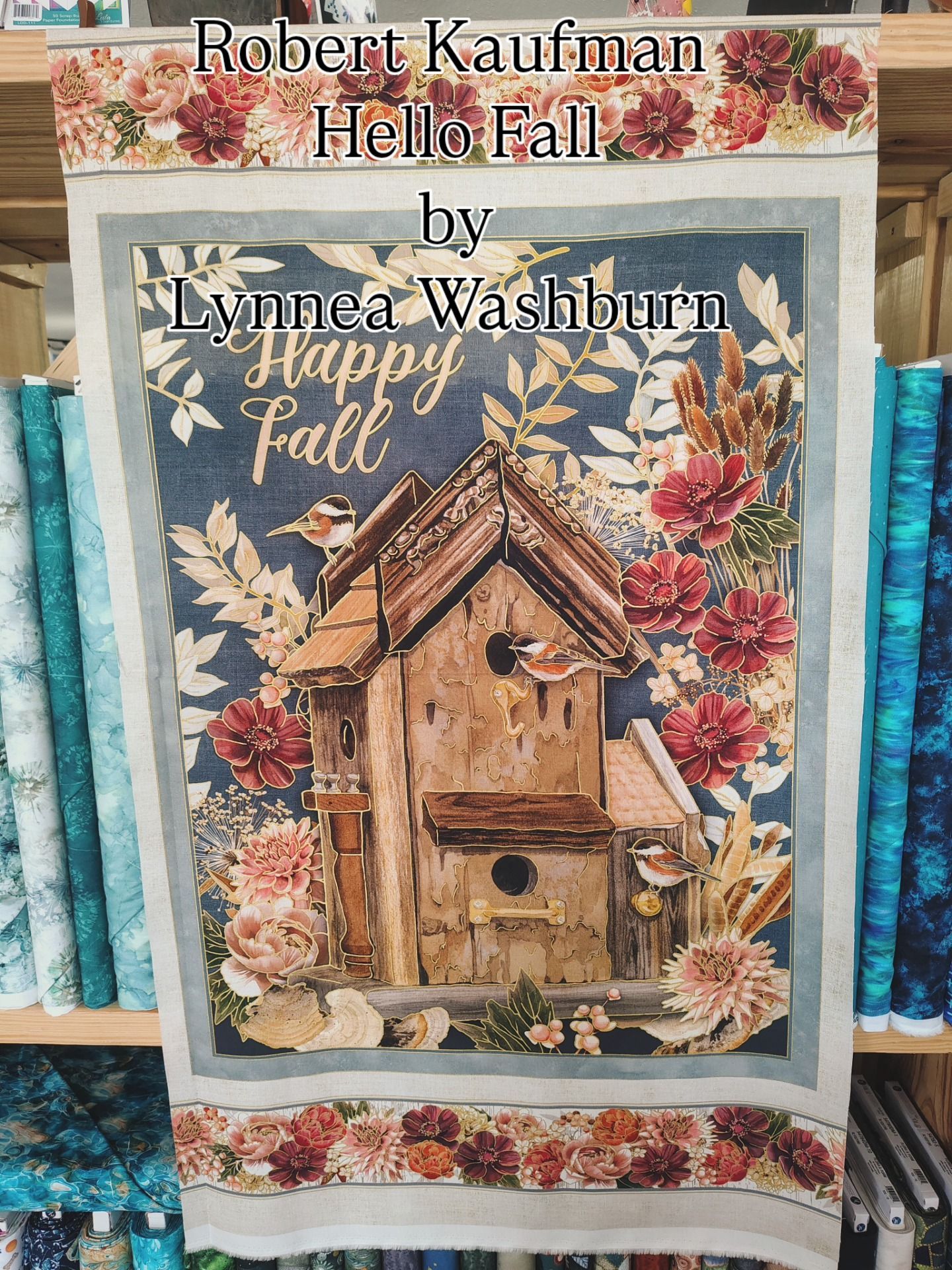 Embroidery sampler of a birdhouse with autumn flowers and text “Happy Fall” on a fabric display panel