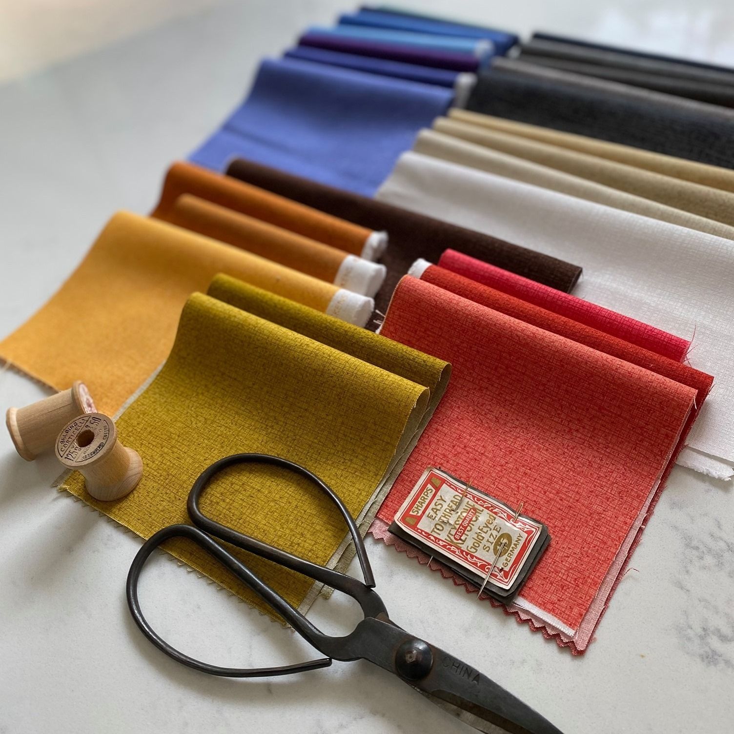 Assorted colorful fabric swatches with scissors and a measuring tape on a table