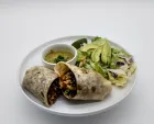 Burrito cut in half, with salsa, avocado salad, and lime on a white plate.