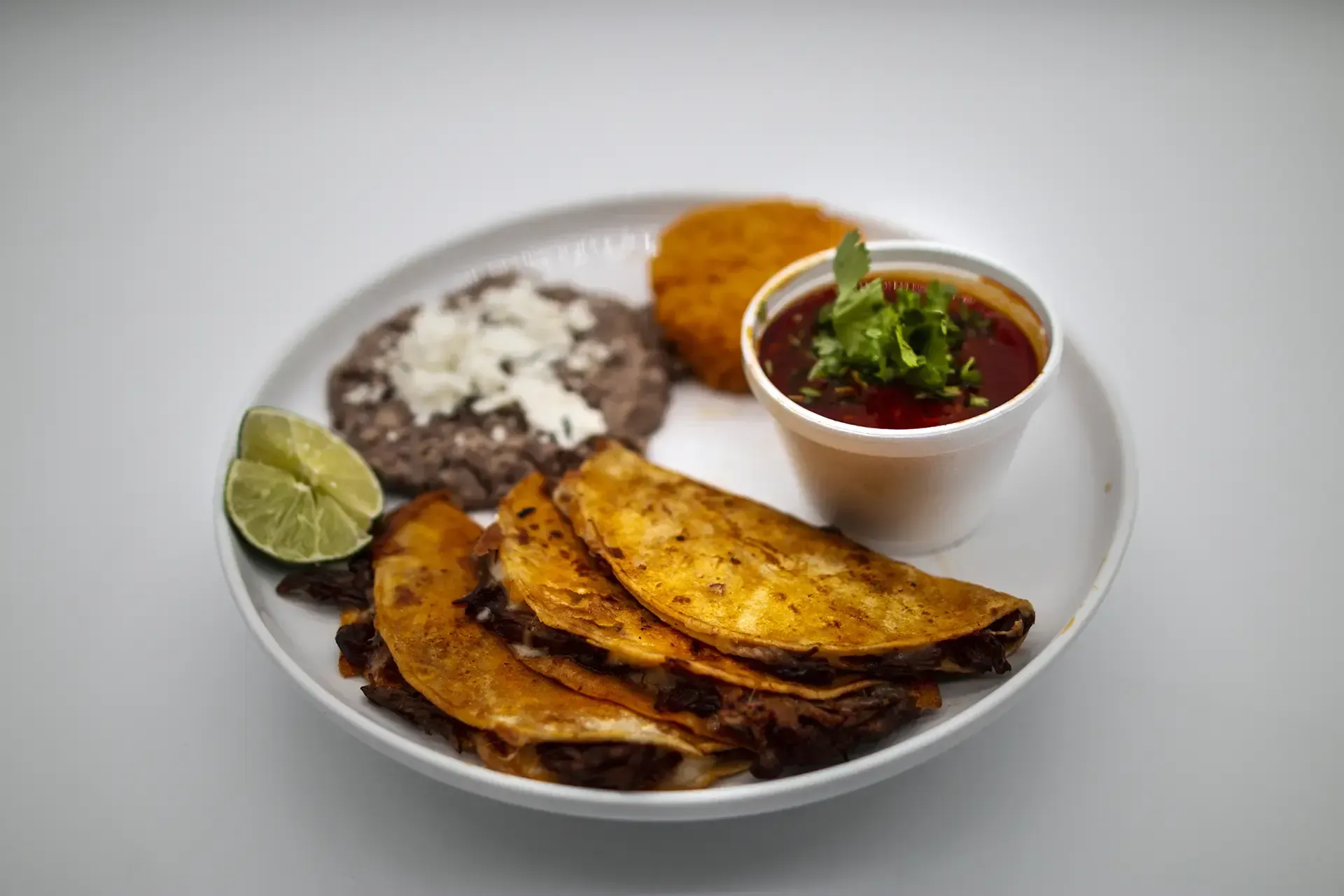 Plate of tacos with beans, a side, salsa, and lime.