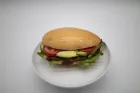 Hamburger with avocado, tomato, and lettuce on a white plate.