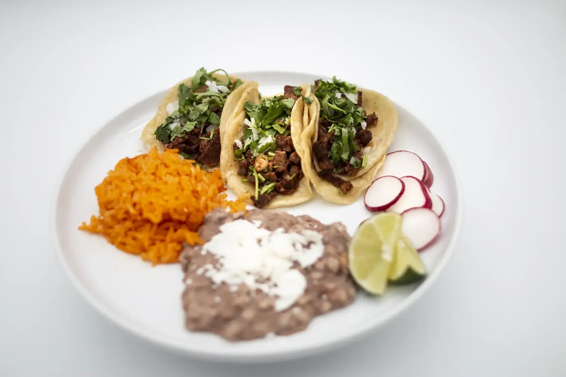 Plate of Mexican food: grilled steak, rice, refried beans with cheese, lime wedges.