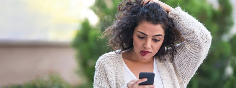 A woman is looking at her cell phone with a surprised look on her face.