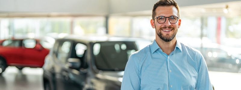 A man is standing in front of a car in a showroom.