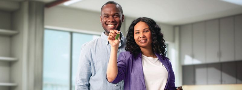 Two smiling people in a bright kitchen, one holding up a small green plant.