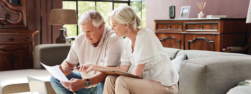 A man and a woman are sitting on a couch looking at a piece of paper.