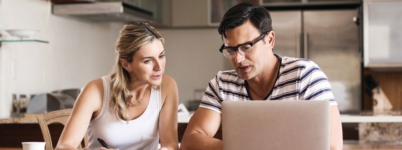 A man and woman in a kitchen looking at a laptop together.