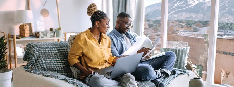 A man and a woman are sitting on a couch looking at papers.