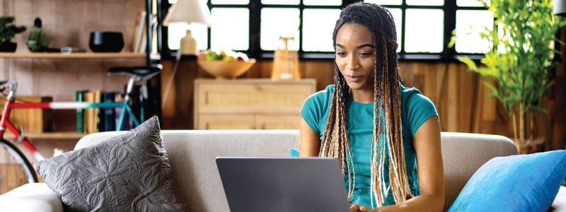 A woman is sitting on a couch using a laptop computer.