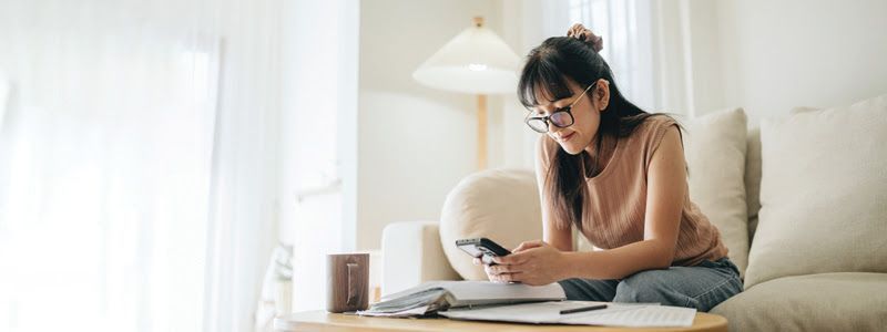 Woman wearing glasses and using her phone, sitting on a couch in a living room.