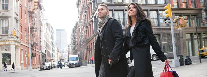 A man and a woman are walking down a city street holding hands.