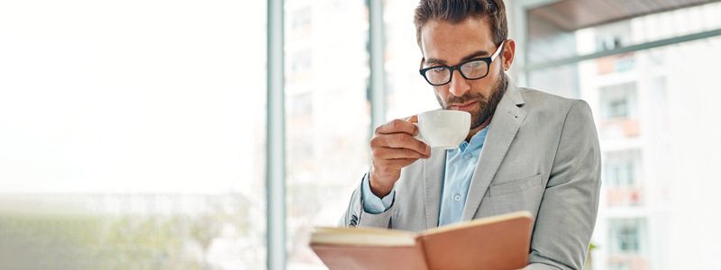 A man is drinking a cup of coffee while reading a book.