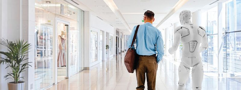 Man walking in a modern building with a robot. They are walking towards the same direction.