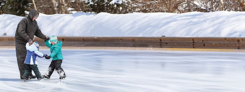 A man and two children are ice skating on a rink.