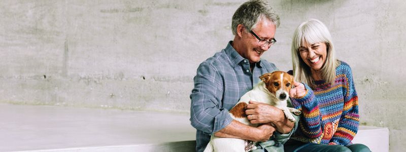 A smiling couple sitting with a dog on a concrete step.