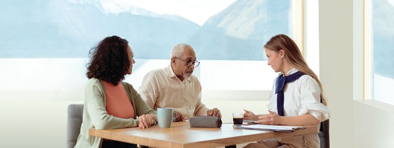 A man and a woman are sitting at a table talking to a woman.