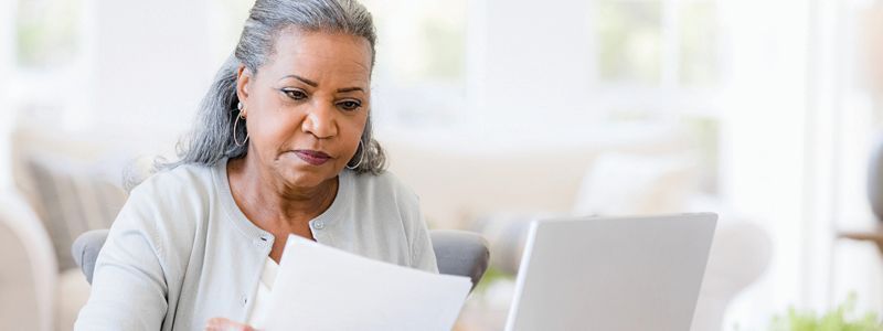 Woman with gray hair looking at papers with a laptop, indoors.