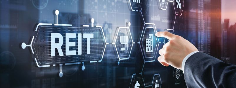 Hand pointing at REIT text with glowing real estate icons on a dark digital background