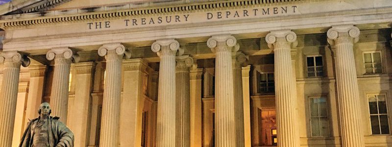 The treasury department building is lit up at night with a statue in front of it.