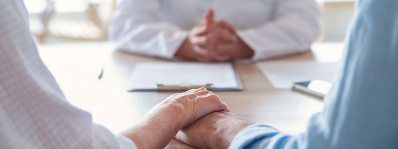 A man and woman are shaking hands while sitting at a table with a doctor.