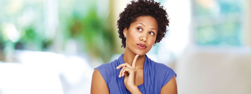 A woman in a blue shirt is thinking with her hand on her chin.