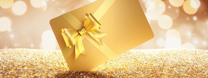 Gold gift box with ribbon and bow on sparkling surface. Bokeh background.