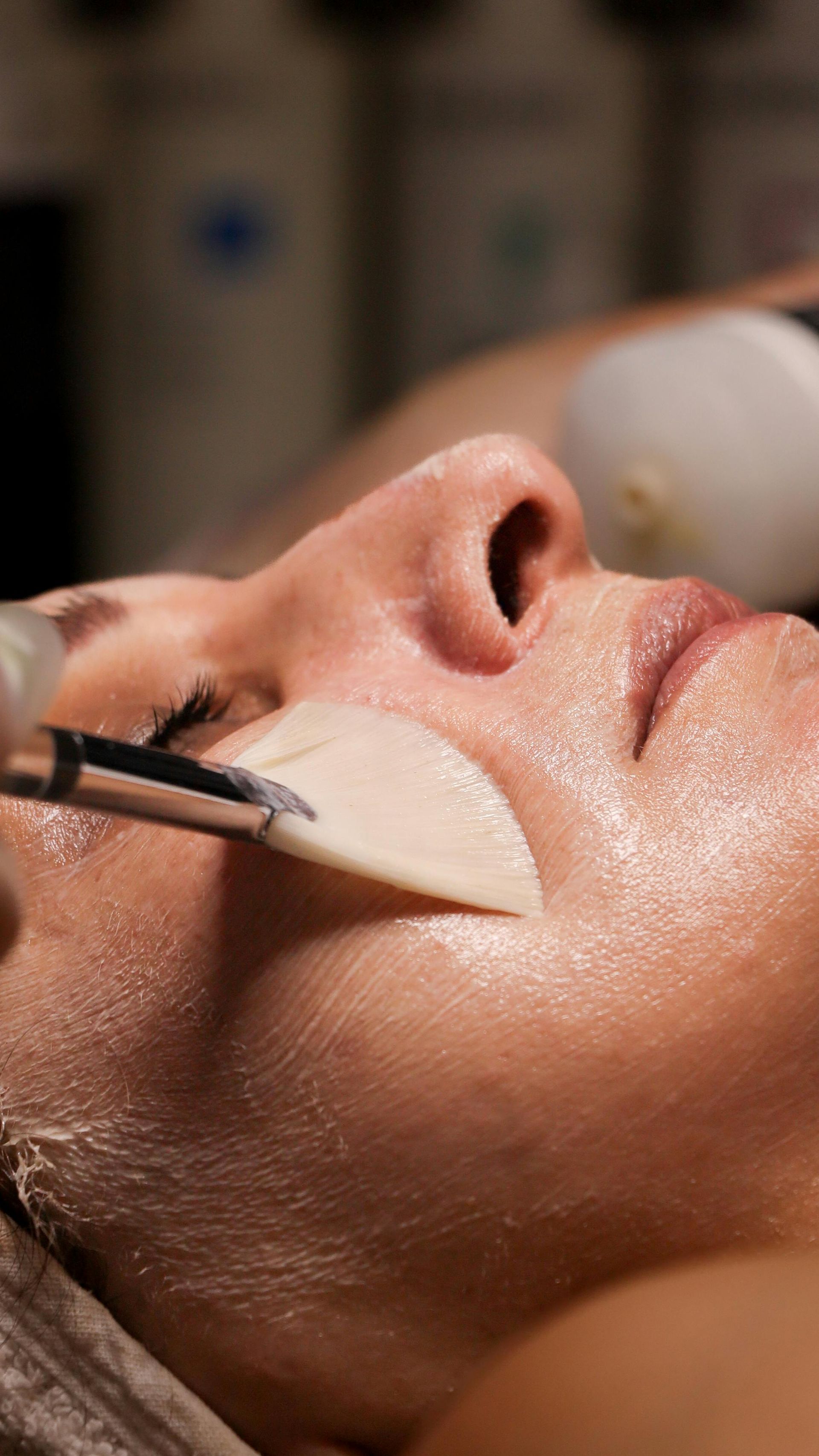 Close-up of a person receiving a facial mask application with a brush in a spa treatment room