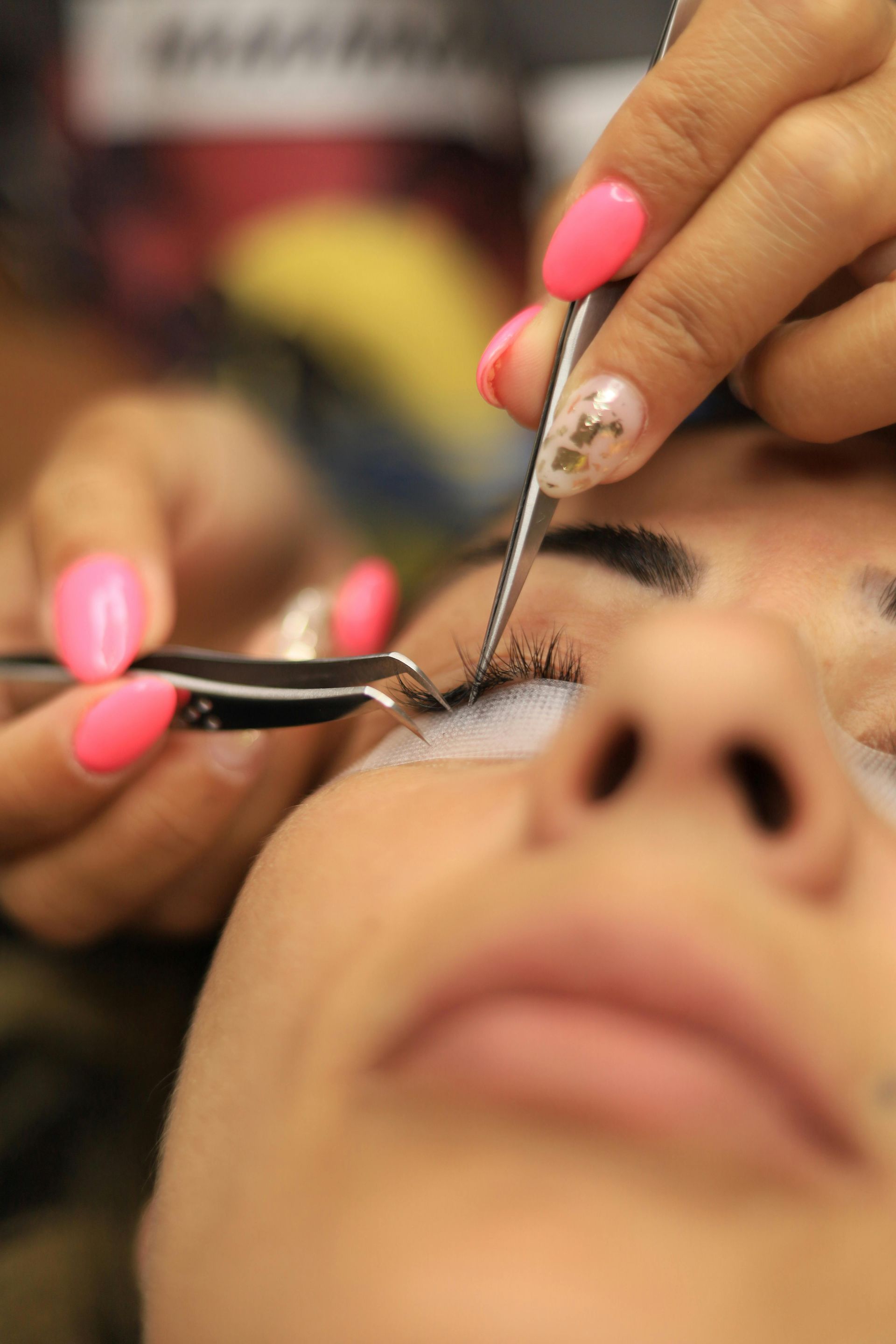 Eyelash technician applying extensions to a client's eye with pink-tipped tools