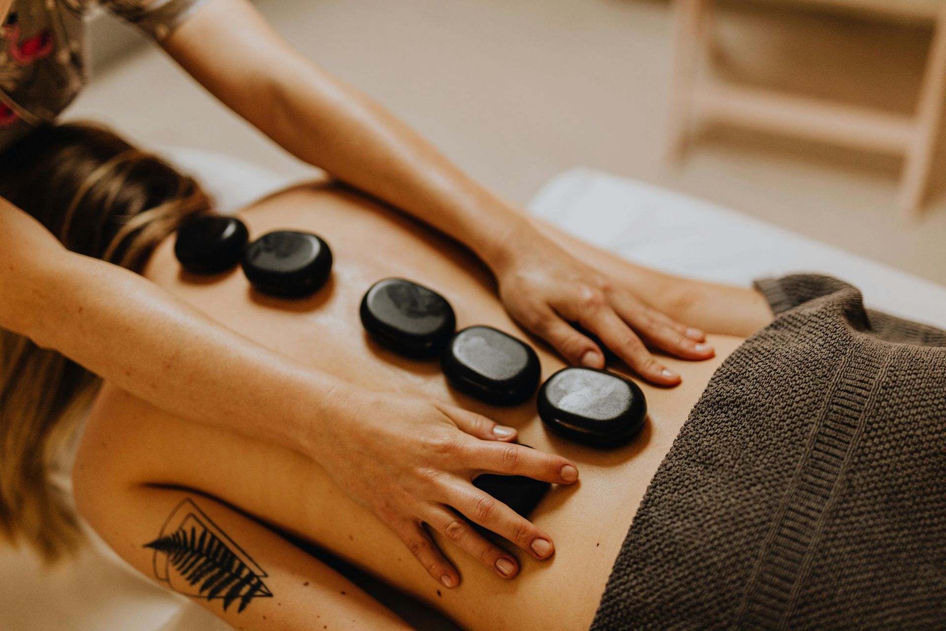 Hot stone massage with four black stones on a client’s bare back, therapist’s hands smoothing oil.