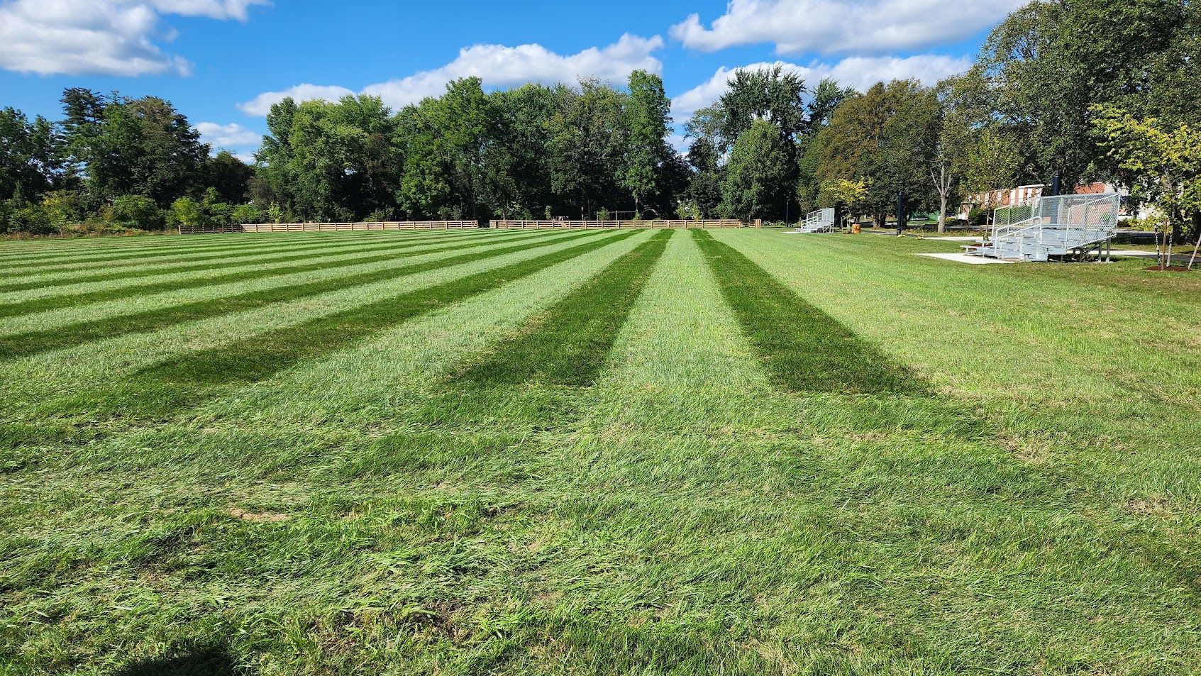 A lush green field of grass is being mowed on a sunny day.