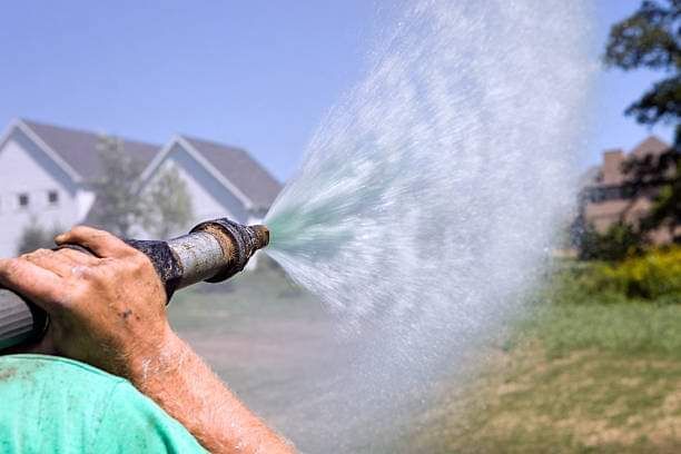 A person is spraying water from a hose in a yard.