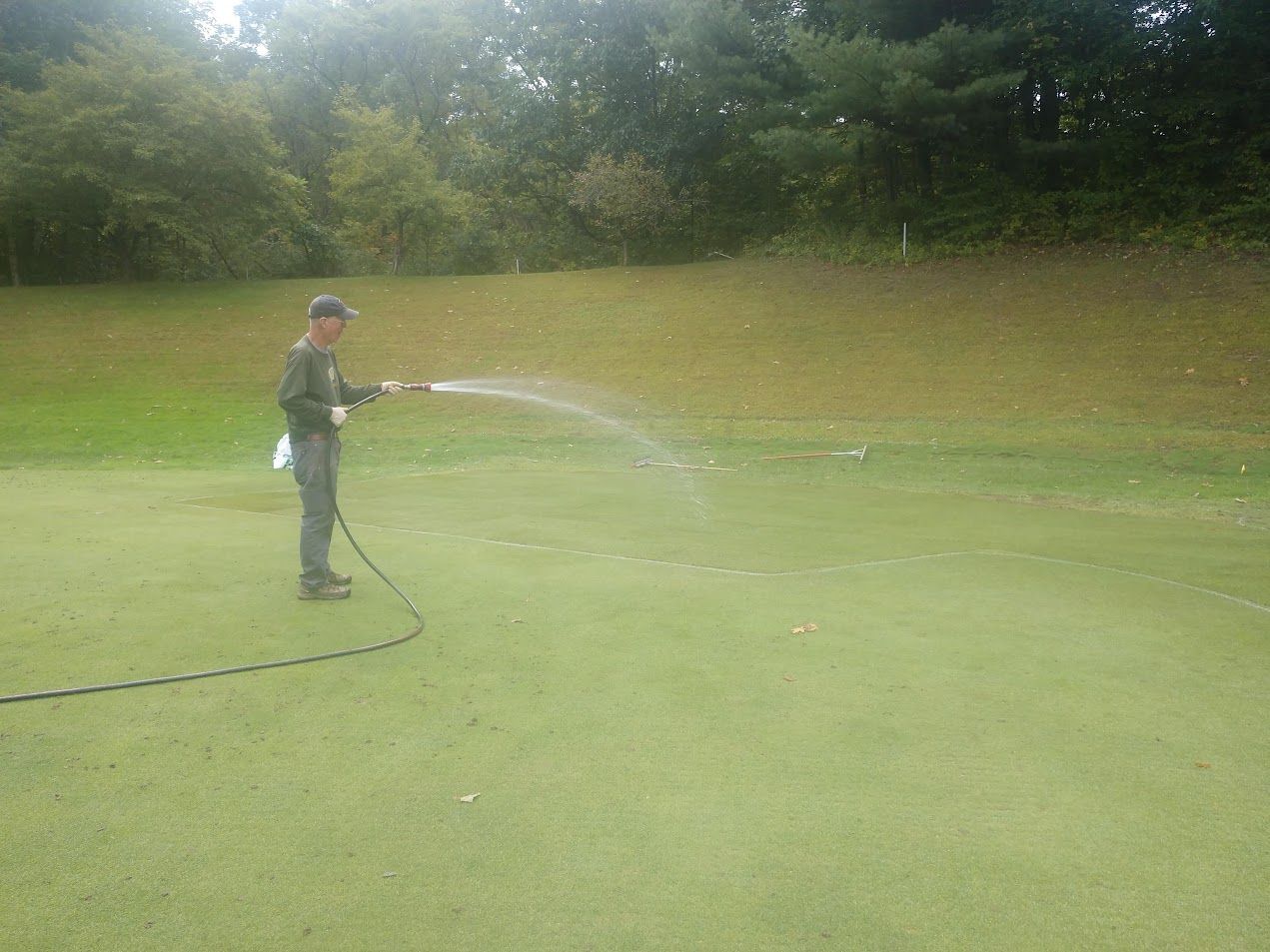 A man is spraying water on a golf course with a hose.
