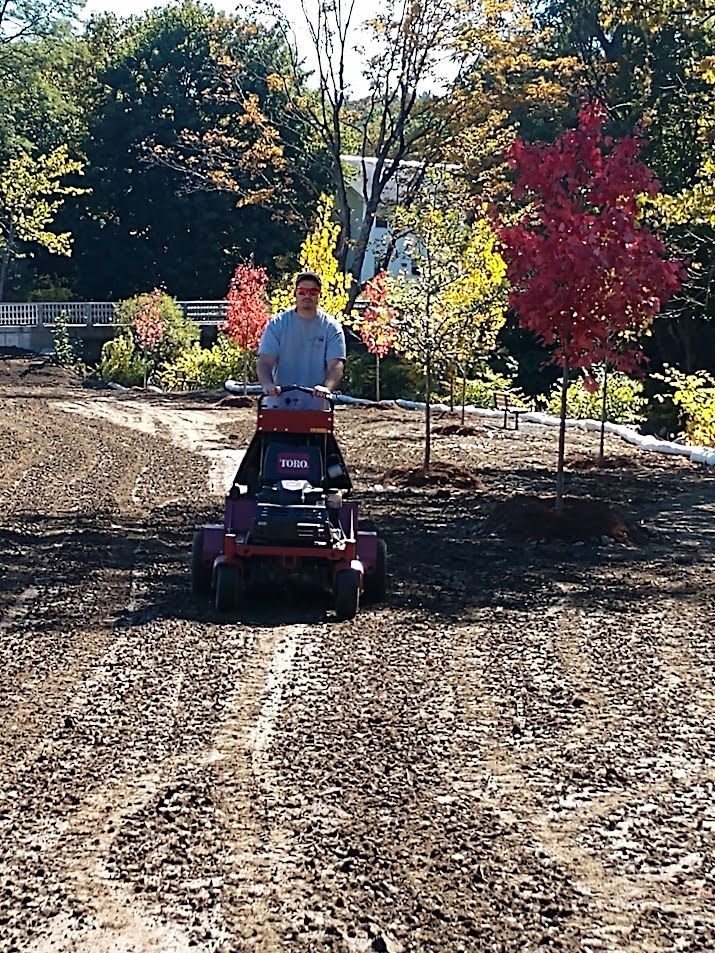 A man is riding a lawn mower through a dirt field.