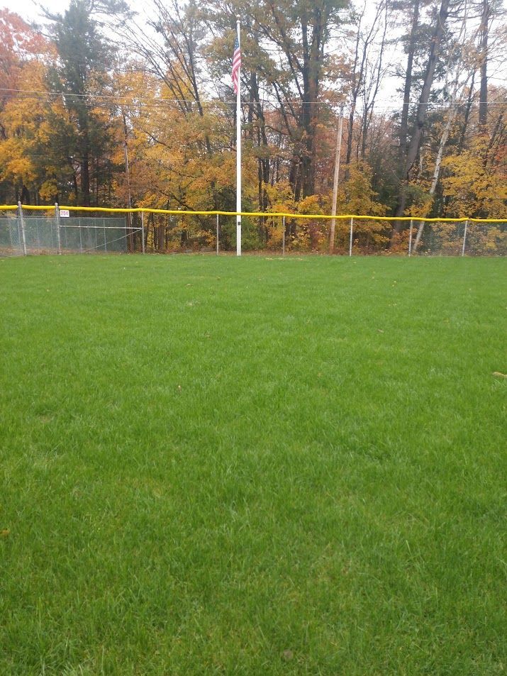 A baseball field with a yellow fence and trees in the background.