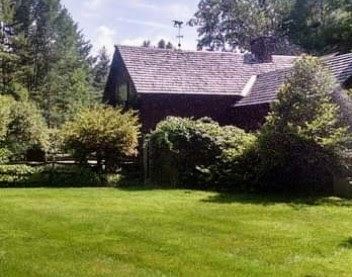 A large house with a large lawn in front of it surrounded by trees.
