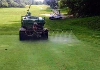 A tractor is spraying water on a golf course next to a golf cart.