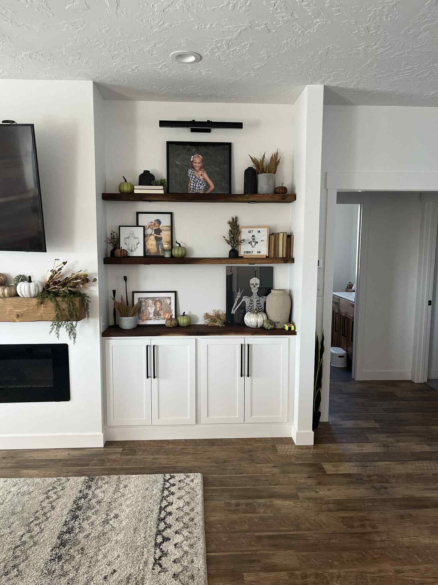 Built-in shelves with decor, including photos and pumpkins, above white cabinets in a living room.