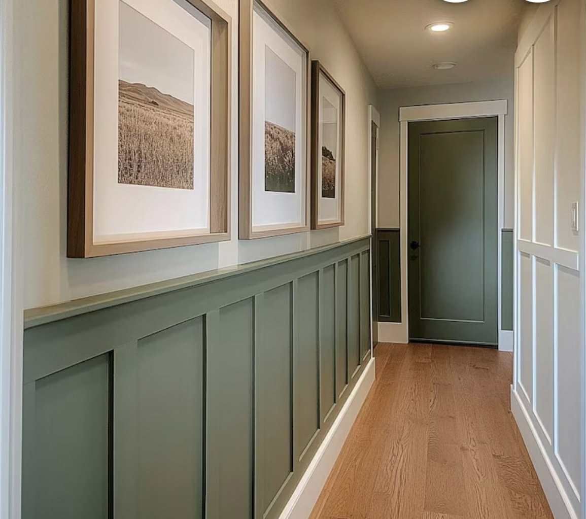 Hallway with olive-green wainscoting and door. Three framed landscape prints hang above. Wood flooring.