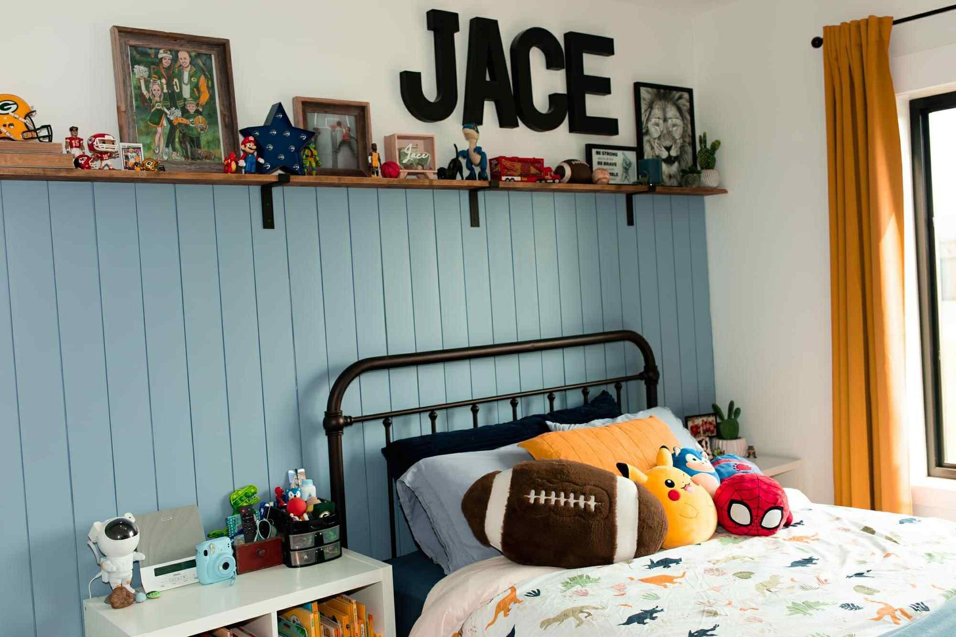 Bedroom with a blue accent wall, a shelf with decor, and a bed with decorative pillows.