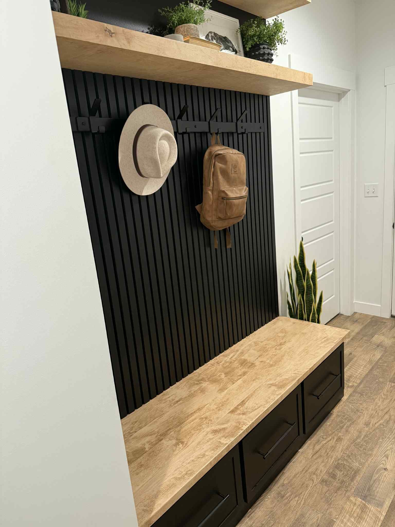 Black slatted entryway with bench, hat, backpack, shelves, and wood flooring.