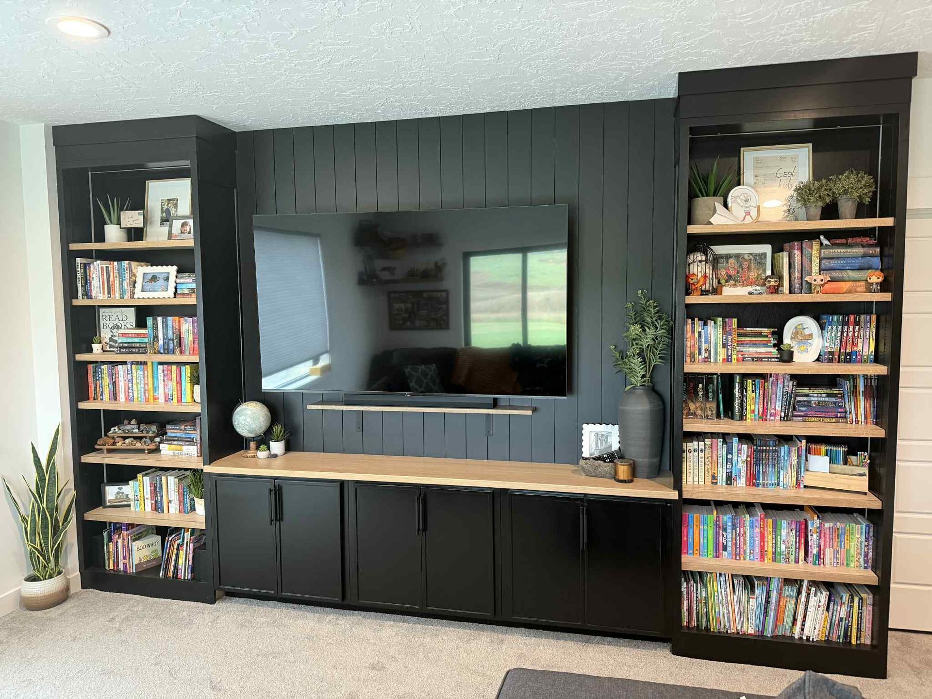 Black media center with a TV, shelving, and cabinets against a dark wall.