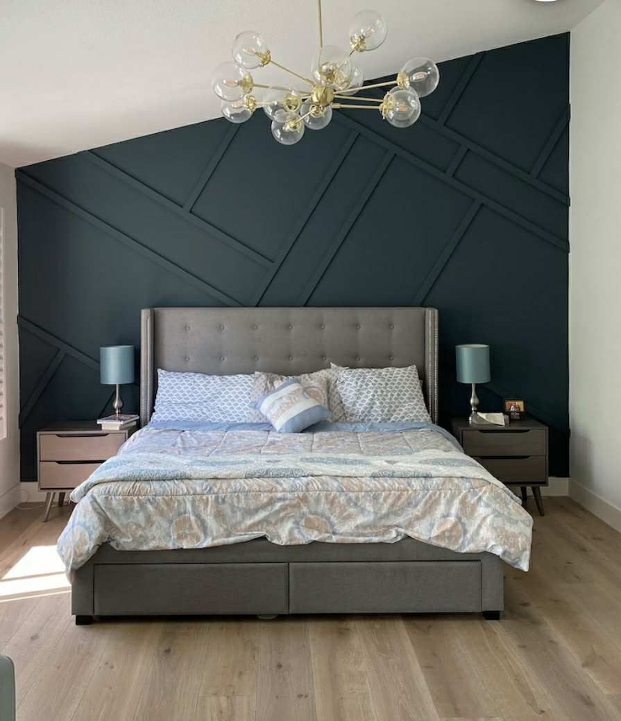Bedroom with blue geometric accent wall, gray bed, wood floors, and a modern chandelier.