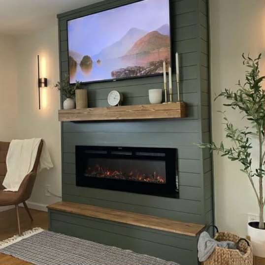 Green shiplap accent wall with a mounted TV, fireplace, wooden mantel, and bench.