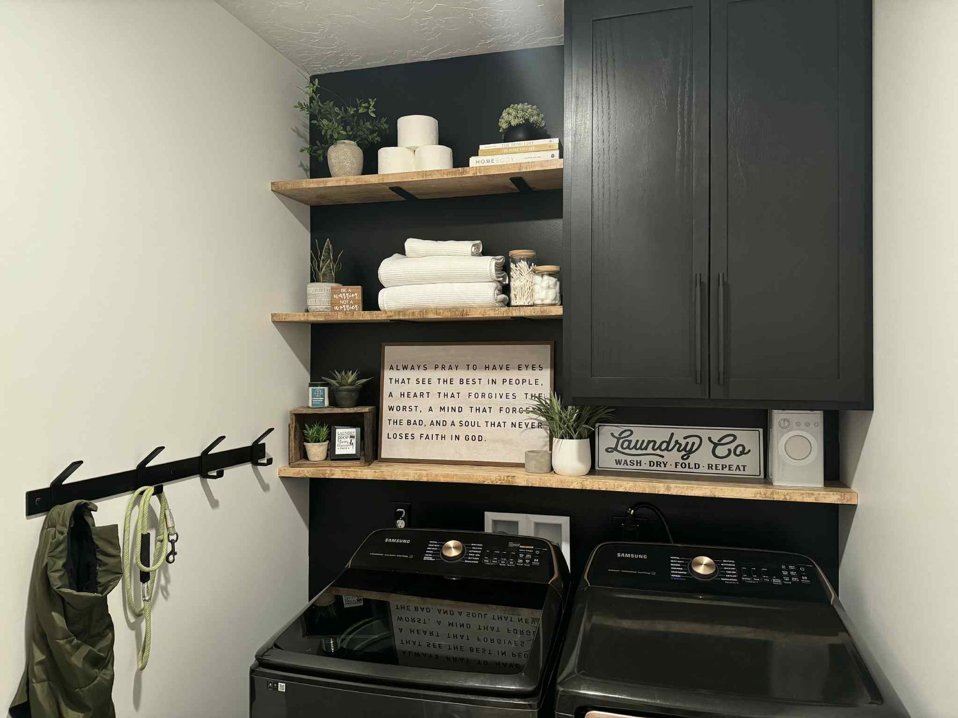 Laundry room with black cabinets, shelves, washer/dryer, and decor.
