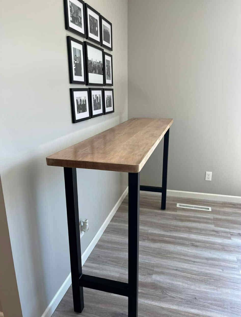 Long wooden table with black legs against a gray wall with framed pictures.