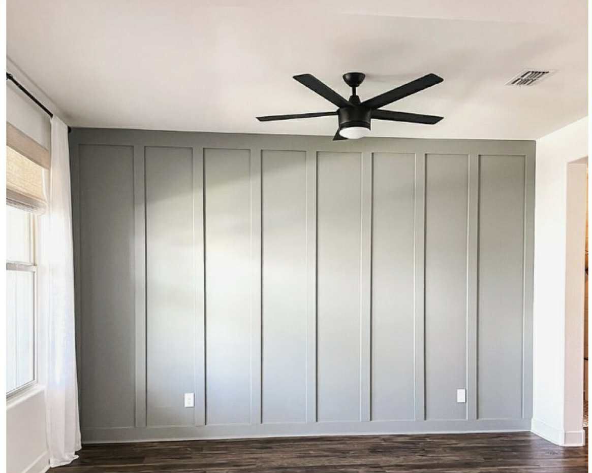 Gray paneled wall with a black ceiling fan in a room.