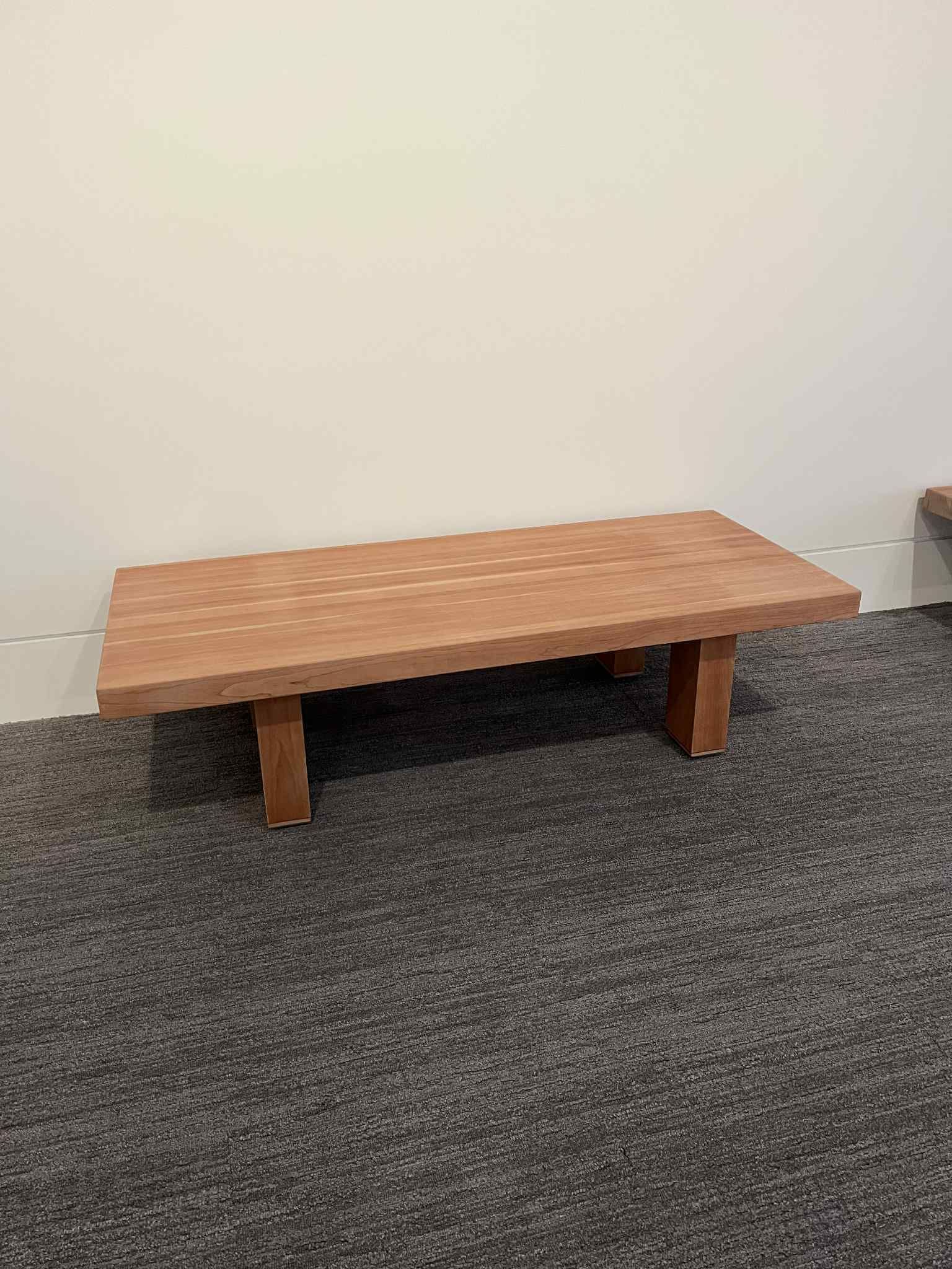 Wooden bench against a white wall and carpeted floor.